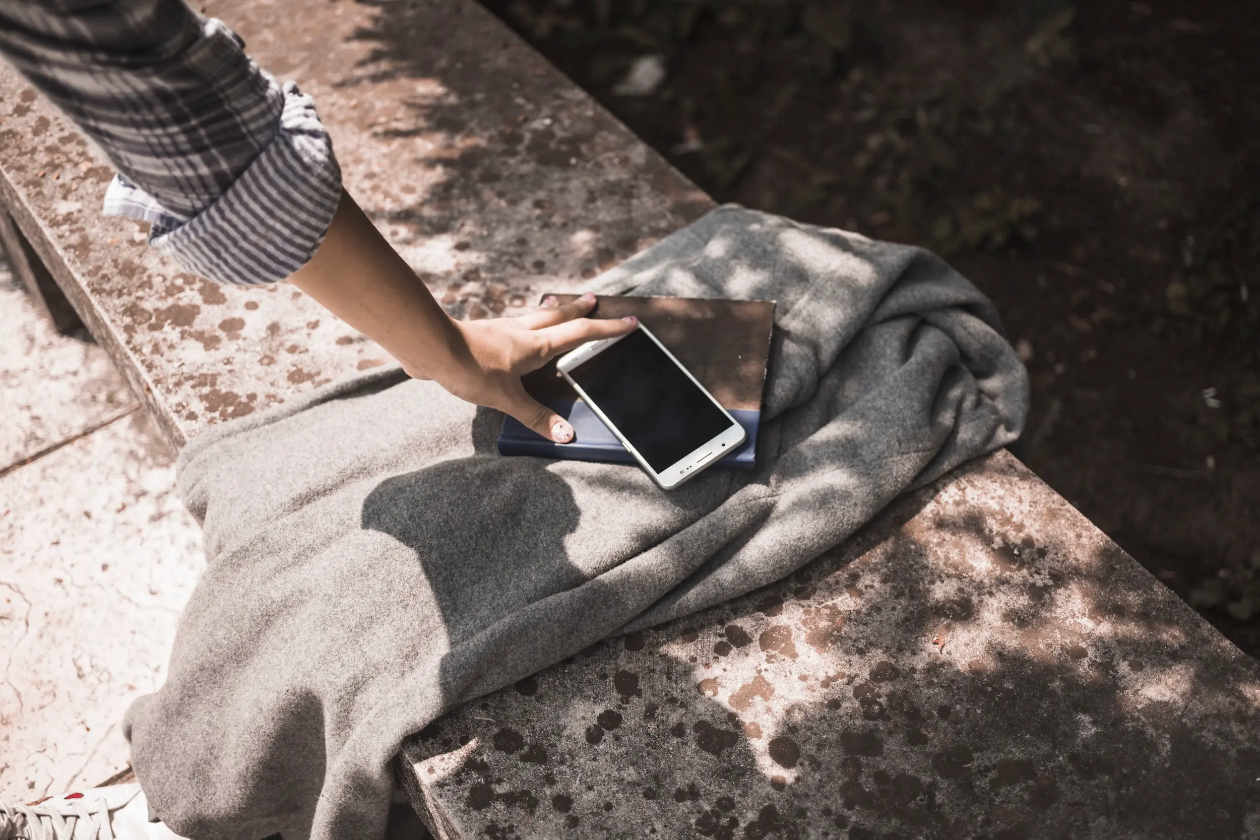 Mensch sitzt in der Sonne mit einem Smartphone