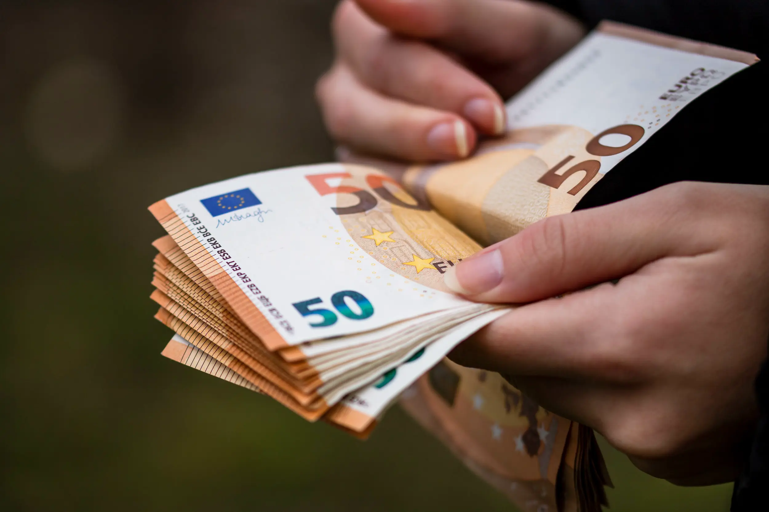 Hände blättern durch einen Stapel von mehreren 50-Euro-Scheinen.