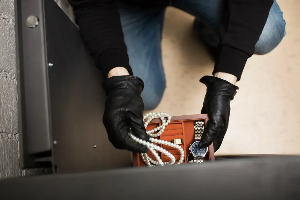 Einbrecher nimmt Schmuck und Wertgegenstände aus einer Schublade.