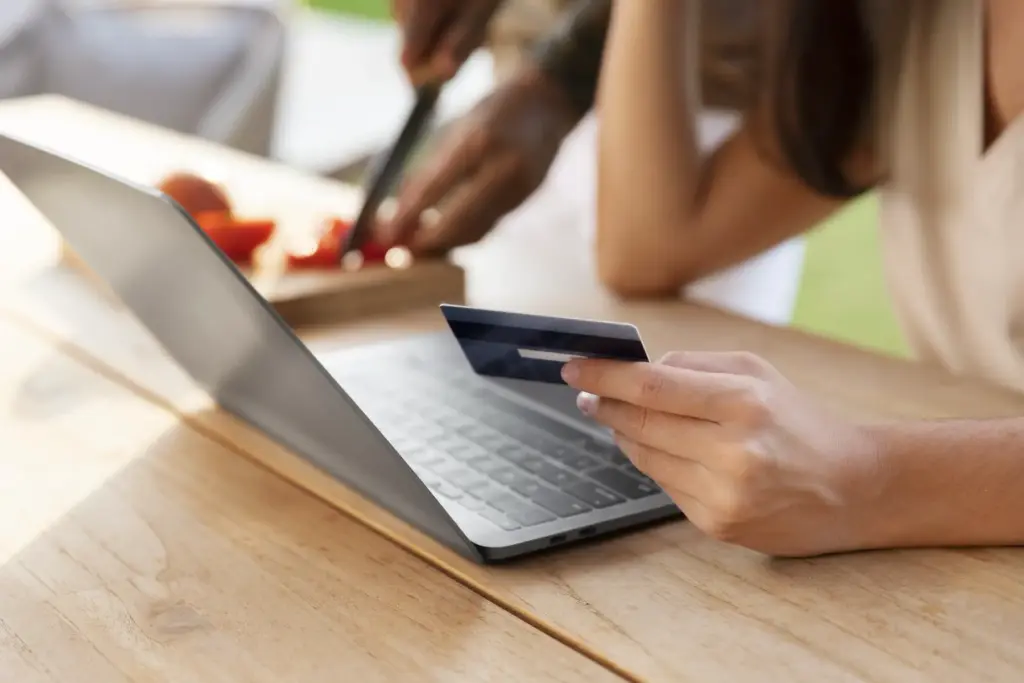 Frau sitzt vor Laptop mit Kreditkarte in der Hand.