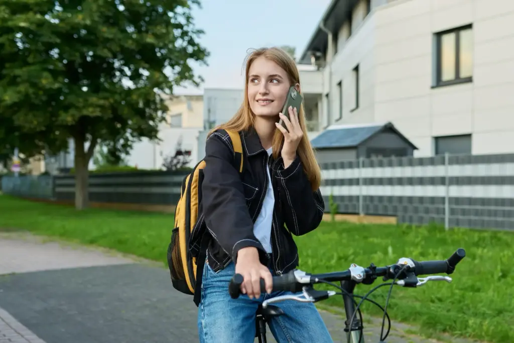Studentin sitzt auf Fahrrad und telefoniert.