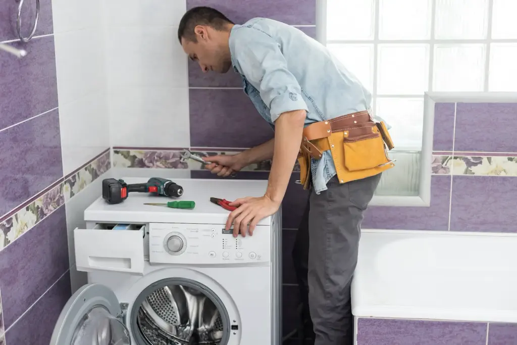 Handwerker schraubt am Wasserschlauch der Waschmaschine herum.